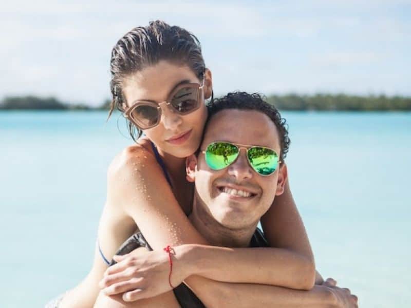 Tymothy Sykes in sunglasses at the beach with attractive young woman, wife Bianca