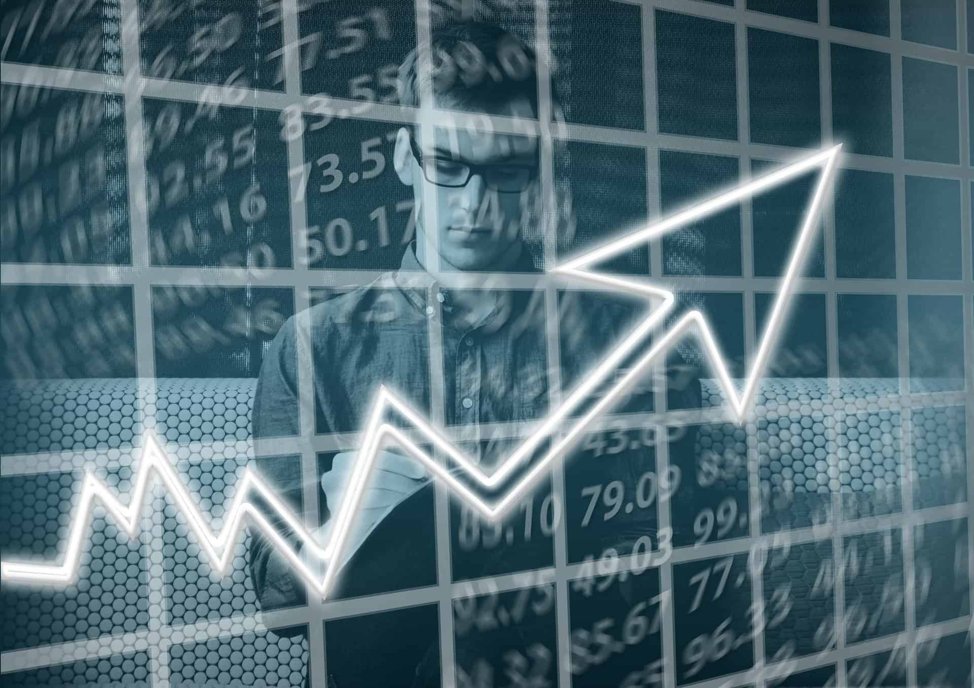 A man who needs books for new investors stands in front of a screen with numbers and an arrow point up.